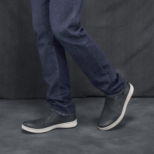 Man in jeans wearing black leather slip-on sneakers.