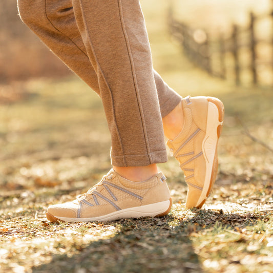 A closeup of compact, lightweight sneakers in a neutral tan shown on foot.
