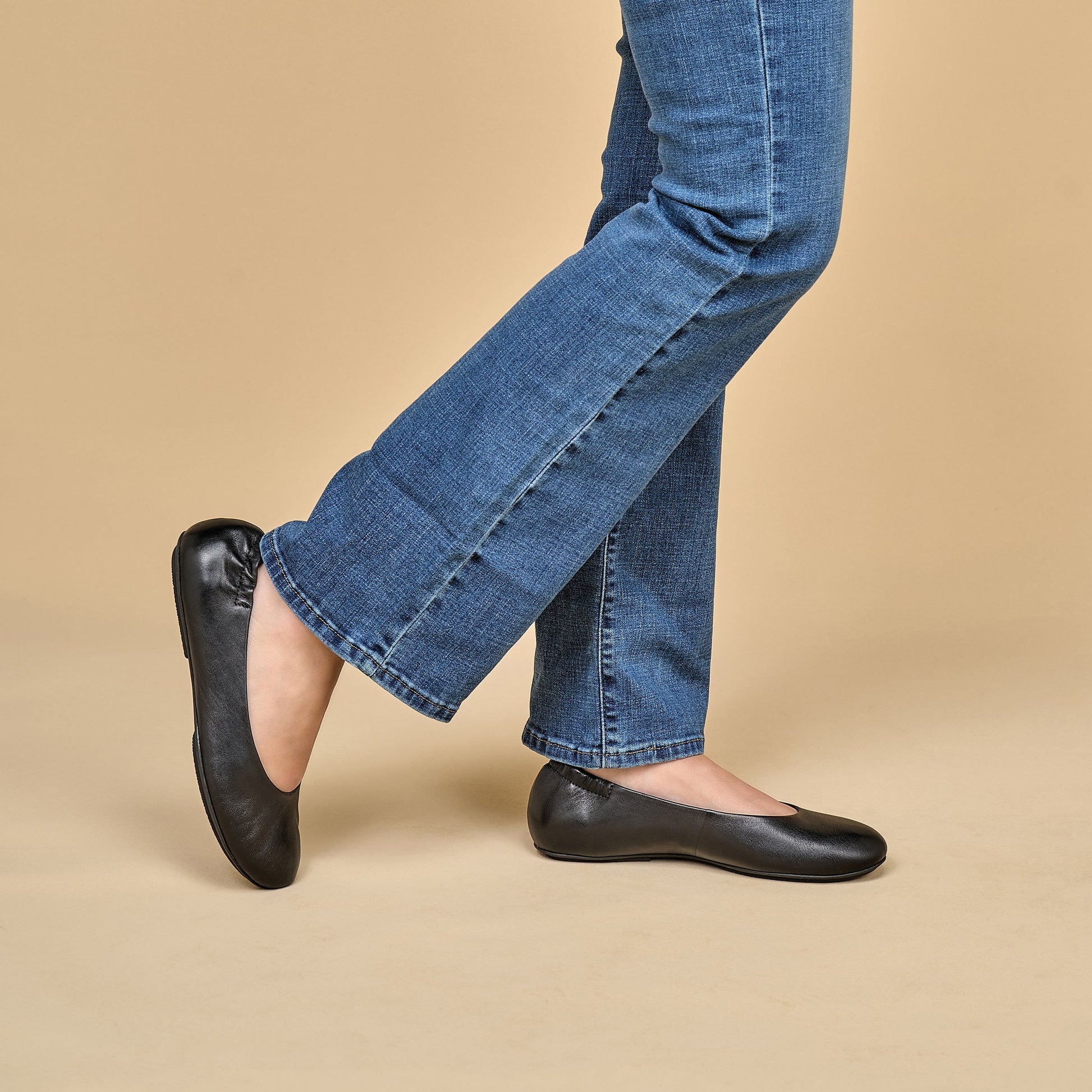 A closeup of black ballerina flats shown on foot.