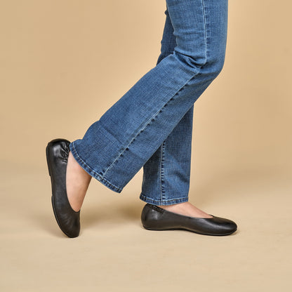 A closeup of black ballerina flats shown on foot.