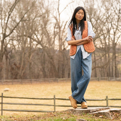 Woman standing outdoors wearing a bright vest, blue button down, jeans, and honey platform Dansko clogs.